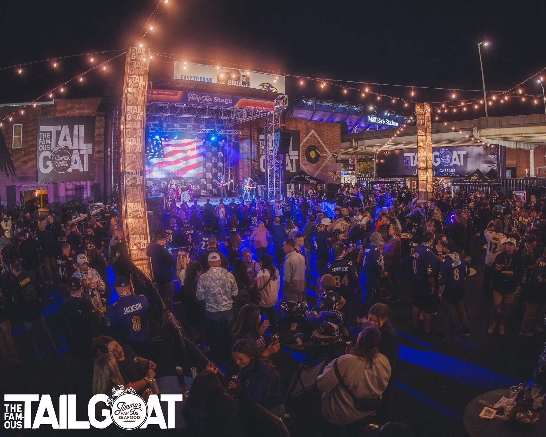 Wide crowd view at a Ravens TailGOAT event with stage visuals