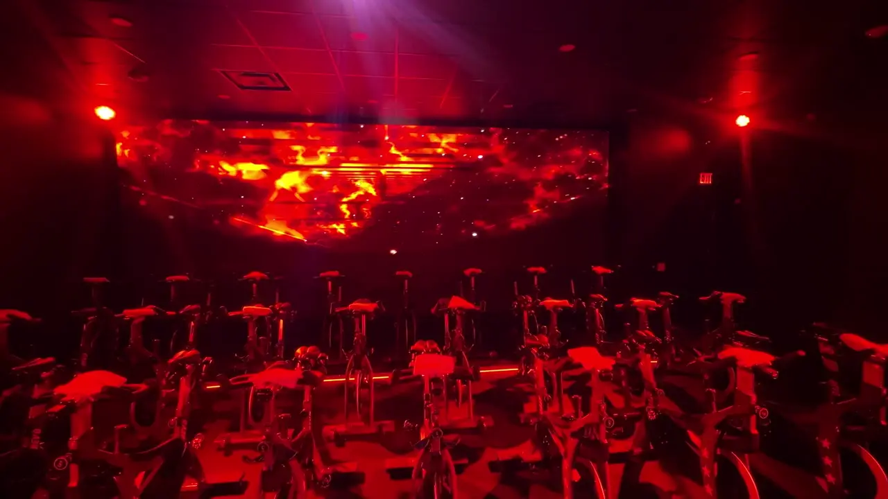 Wraparound LED wall lit magenta behind rows of spin bikes in the REVd cycle room