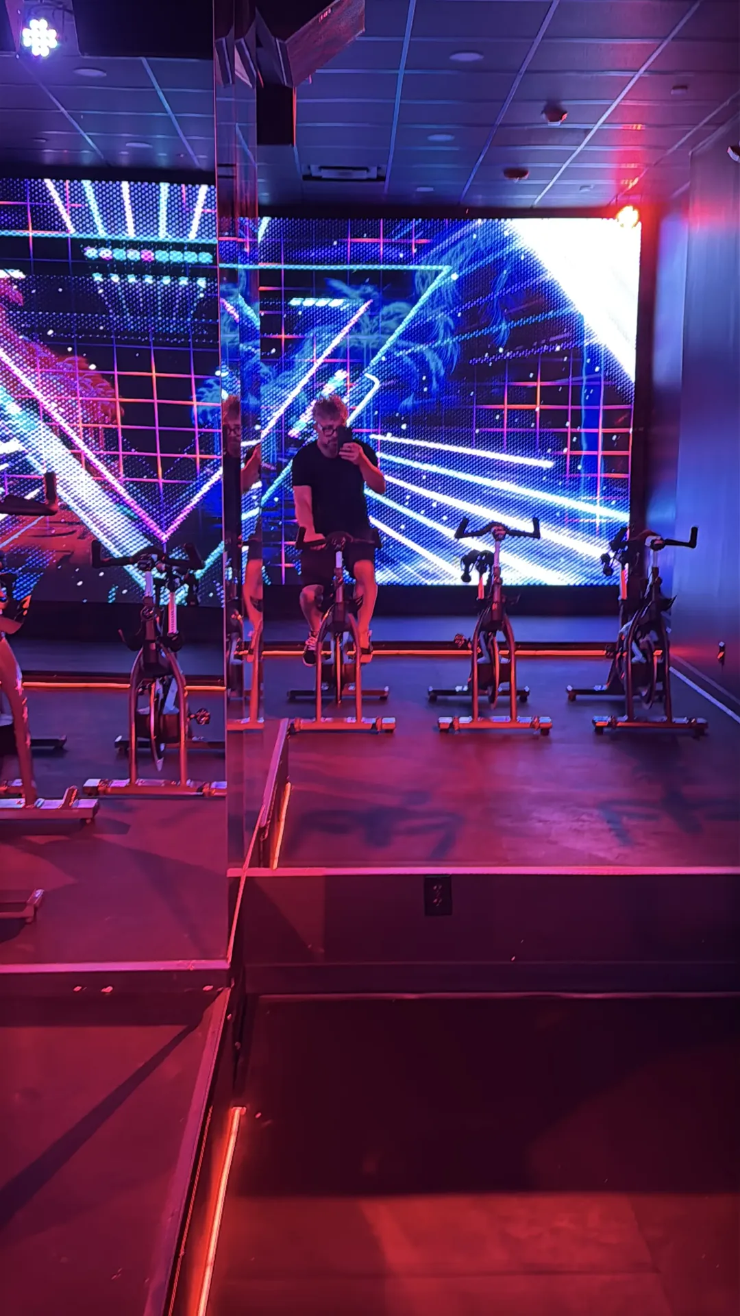 The LED wall running synthwave graphics behind the bikes, caught with its rider in the mirrored wall.