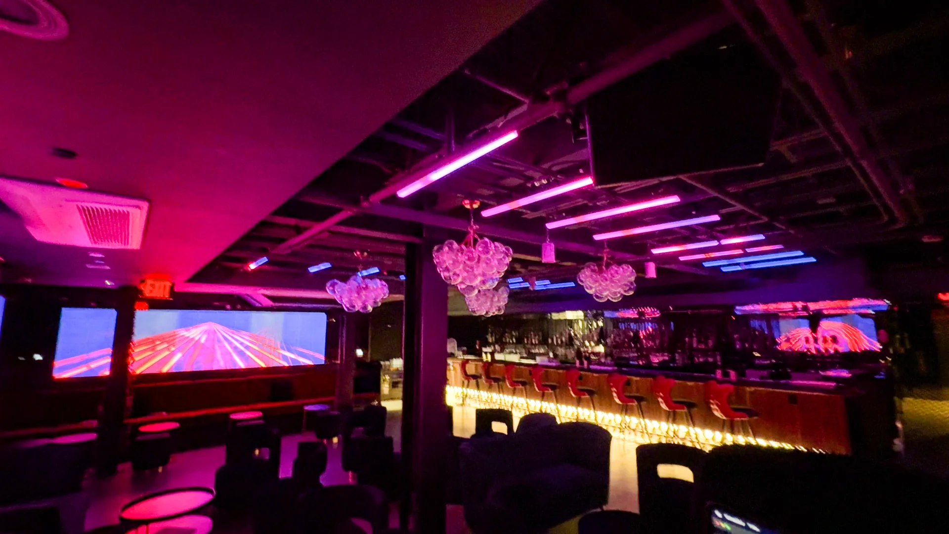 The bar under warm light with pink content running on the screens above