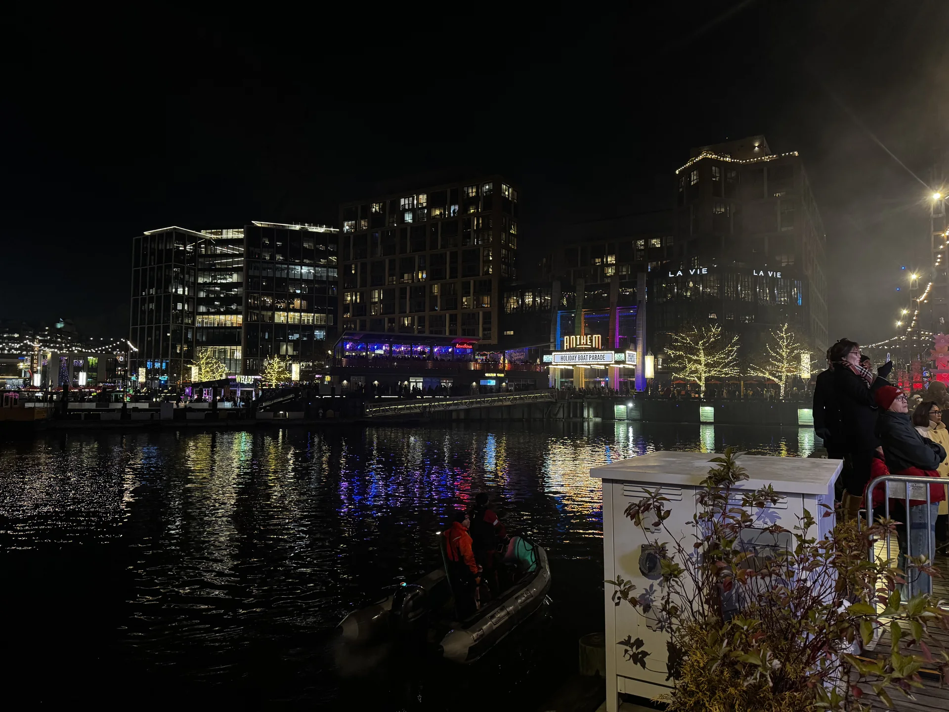 Spectators at the rail with the lit waterfront and channel behind them