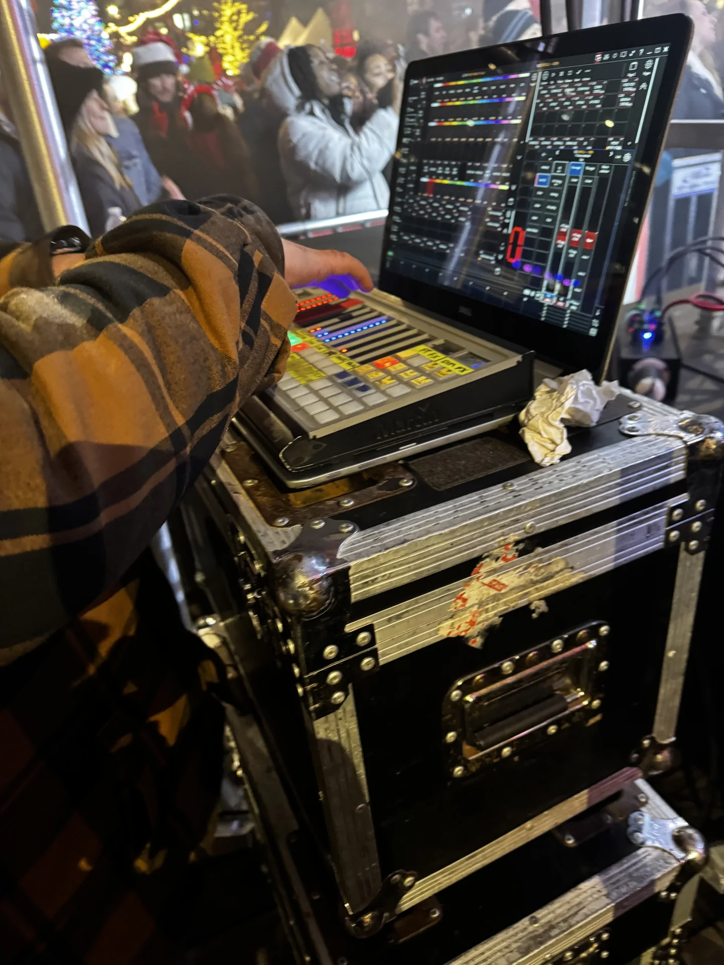 Hand triggering clips on a laptop running a playback grid, crowd visible beyond