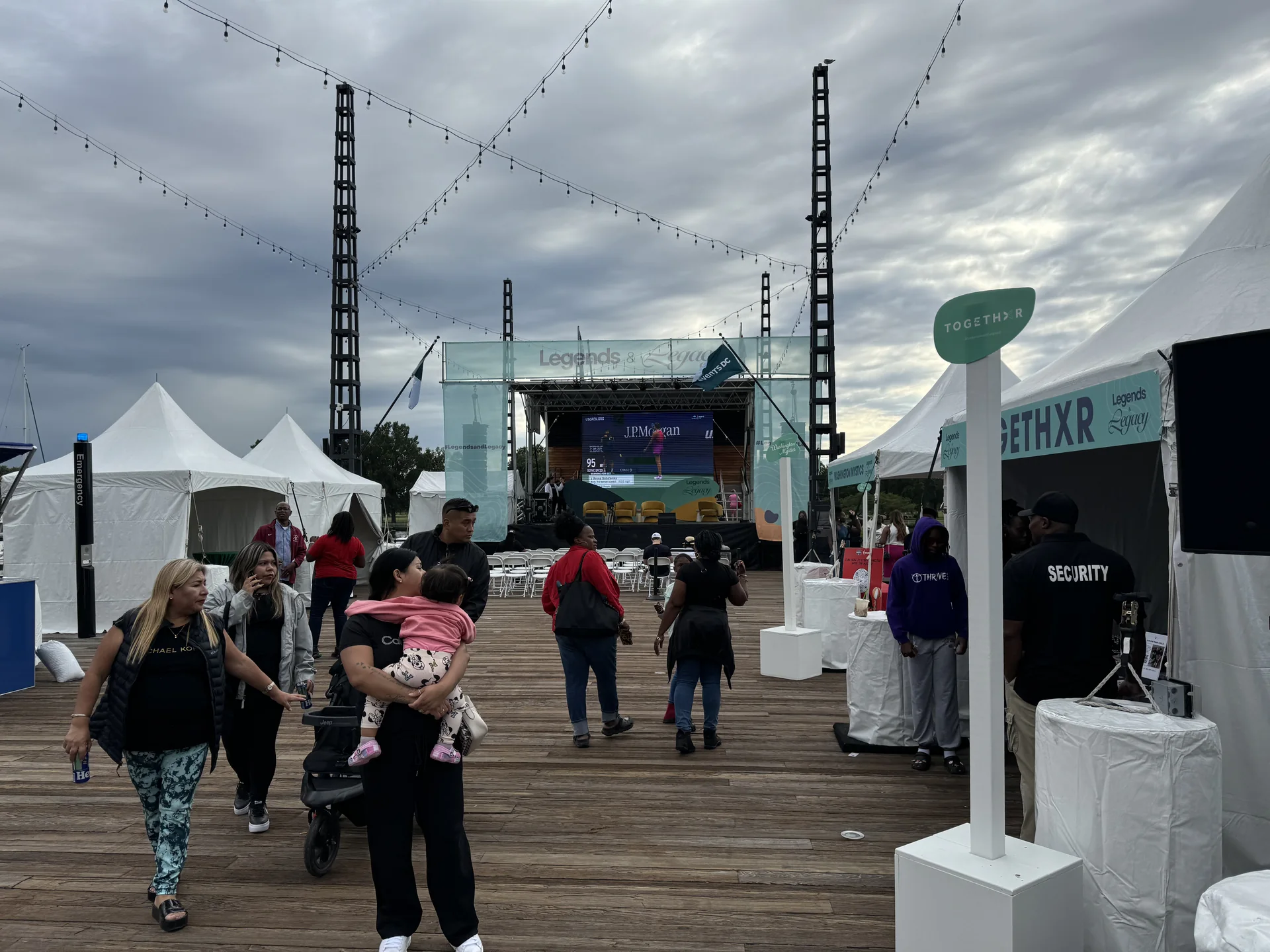 Attendees walking the pier past event tents toward the stage