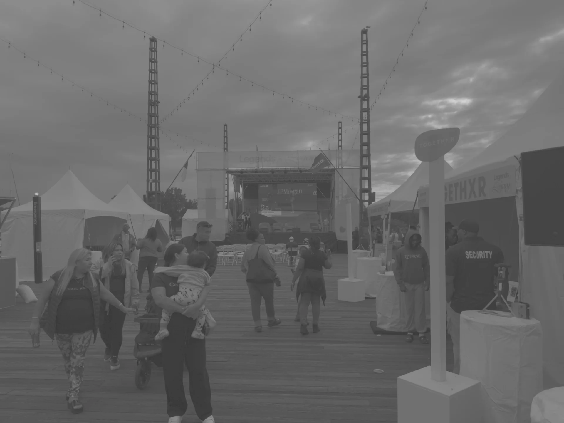 Pedestrians and tents on the boardwalk with the screen tower visible in the distance
