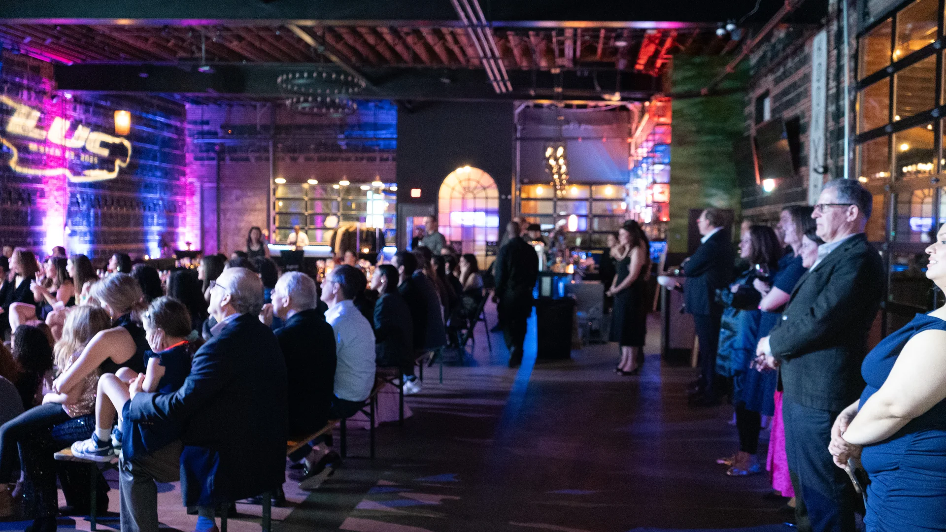 Full crowd inside an industrial venue with the LUC mark projected on the brick wall