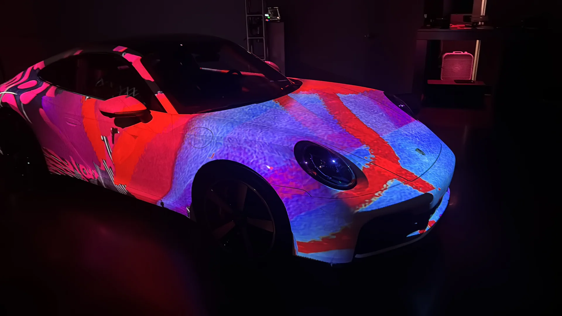 A Porsche 911 in a dark room with red and blue content projected across its body