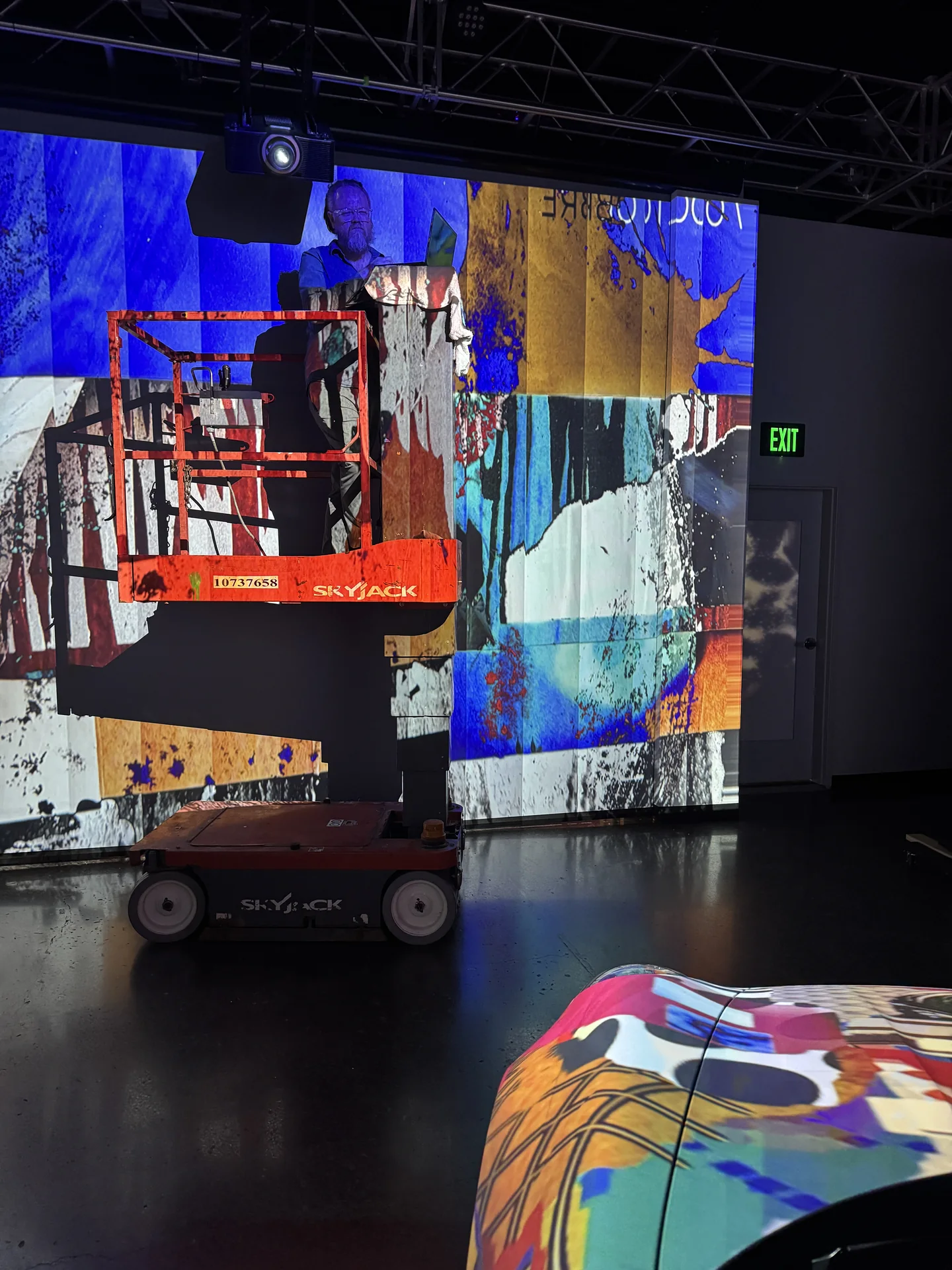 A scissor lift in the room in front of a wall running dense colour content