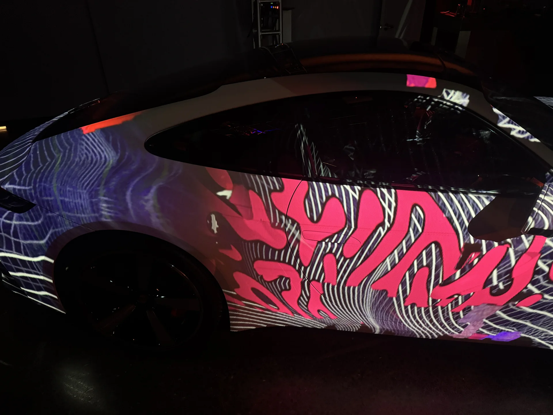 A Porsche in the studio with pink and white pattern projected along its flank