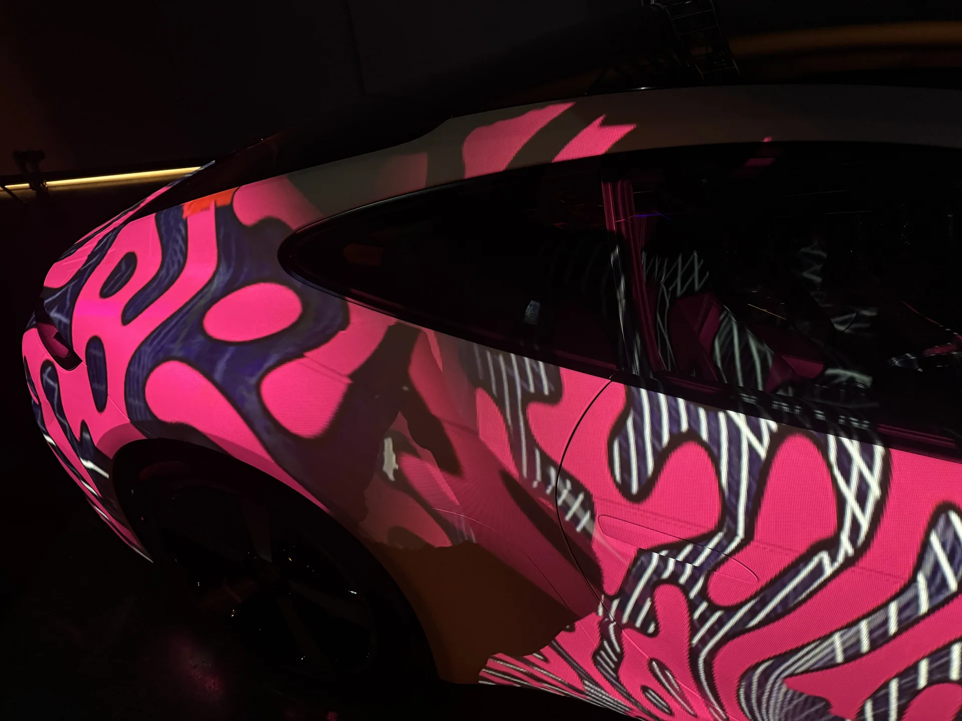 Close view of a Porsche with bold pink graphic content projected across the rear quarter